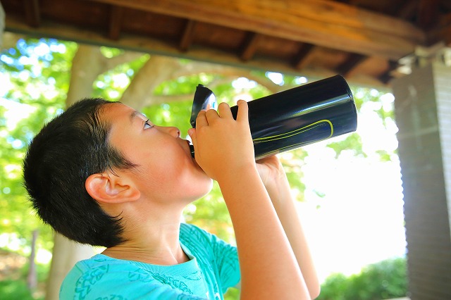 水筒で水分補給をする男子児童の画像