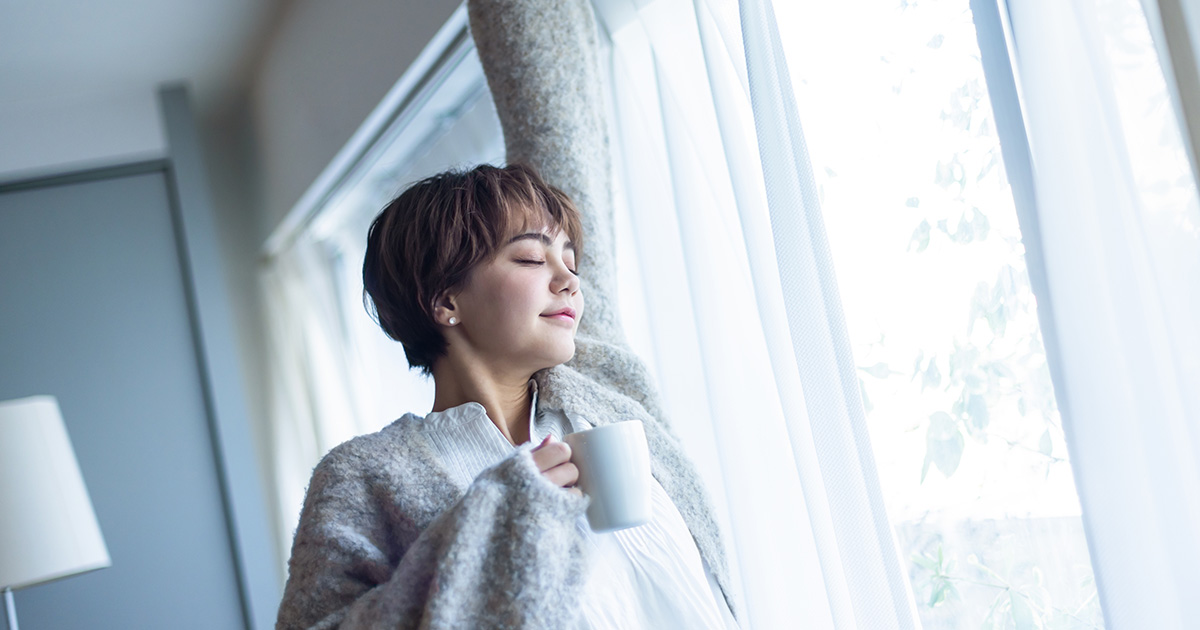 窓辺で白湯を飲む女性の画像